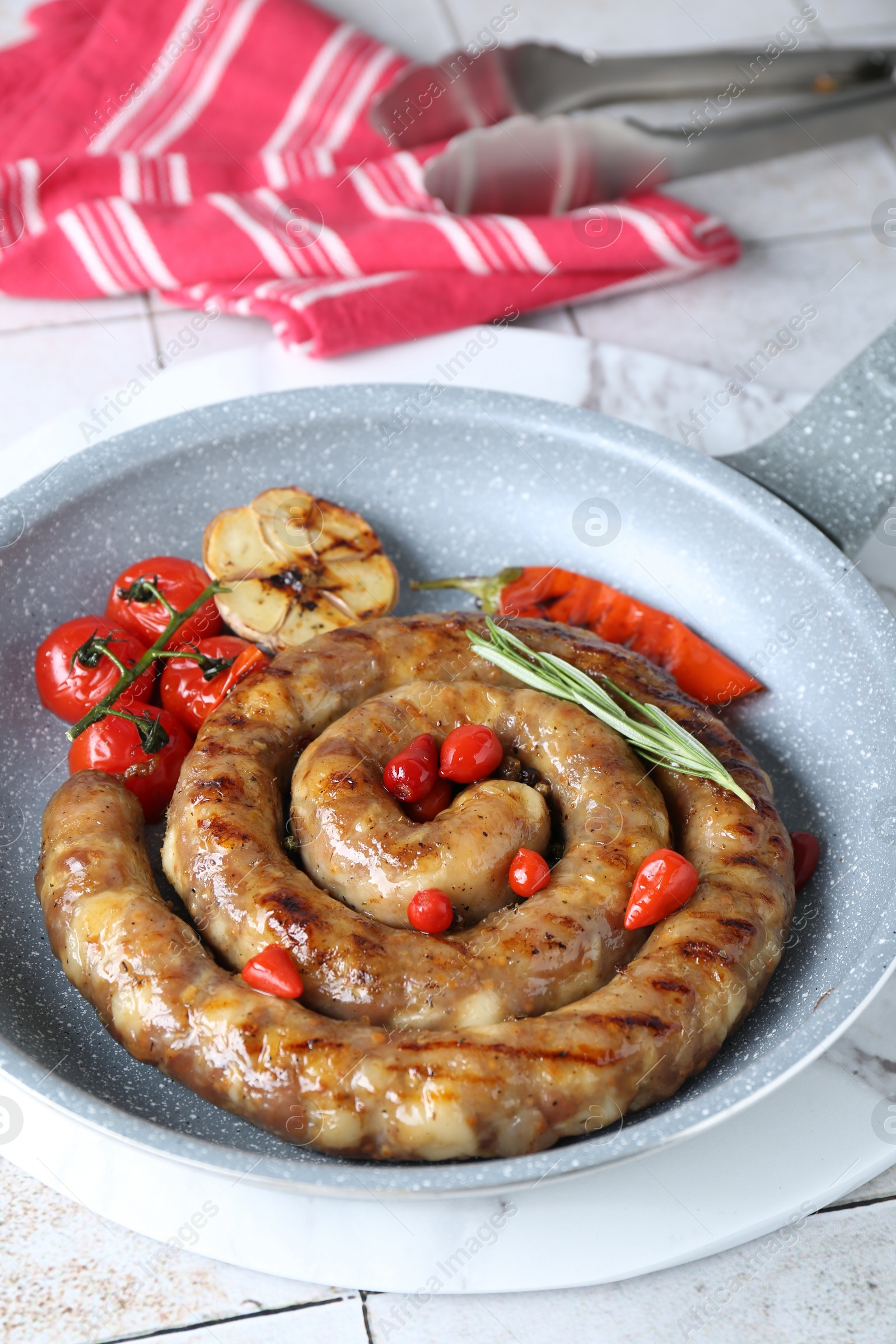 Photo of Delicious homemade sausage with garlic, tomatoes, rosemary and chili in frying pan on light tiled table, closeup