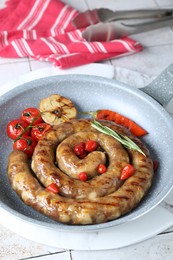 Delicious homemade sausage with garlic, tomatoes, rosemary and chili in frying pan on light tiled table, closeup