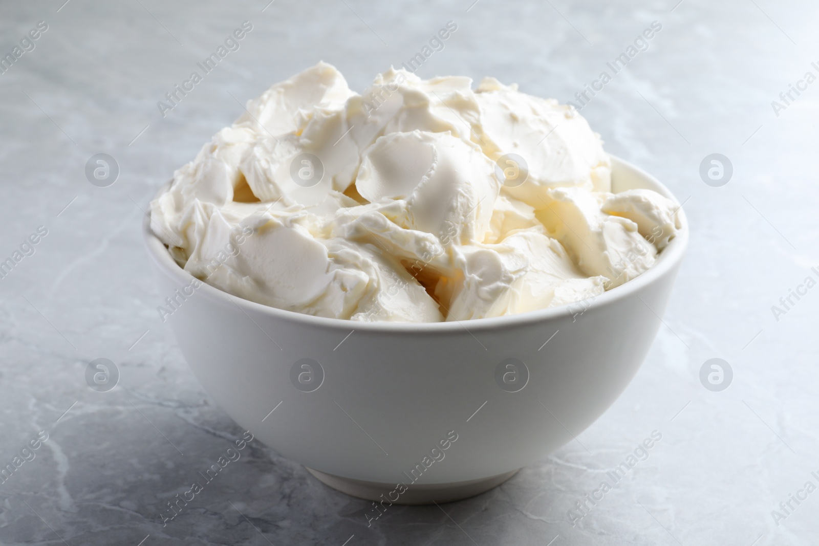 Photo of Bowl of tasty cream cheese on light grey marble table, closeup