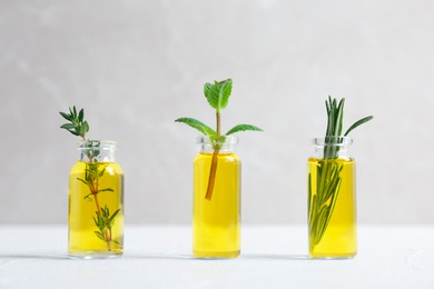 Bottles with essential oils and fresh herbs on light background