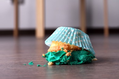 Photo of Dropped cupcake with cream on wooden floor at home, closeup. Troubles happen