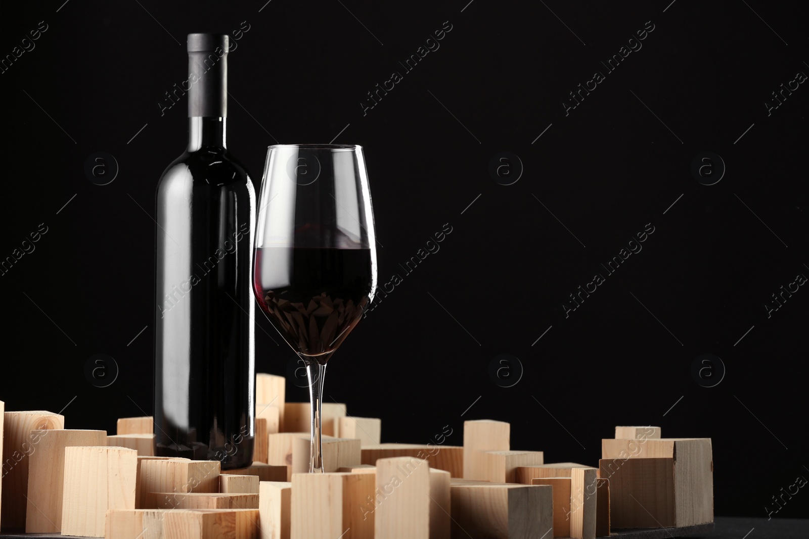 Photo of Stylish presentation of red wine in bottle and wineglass on black background, space for text