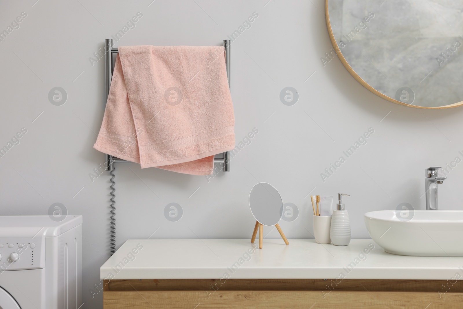 Photo of Heated rail with pink towel on white wall in bathroom