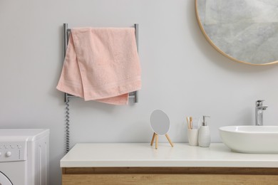Photo of Heated rail with pink towel on white wall in bathroom