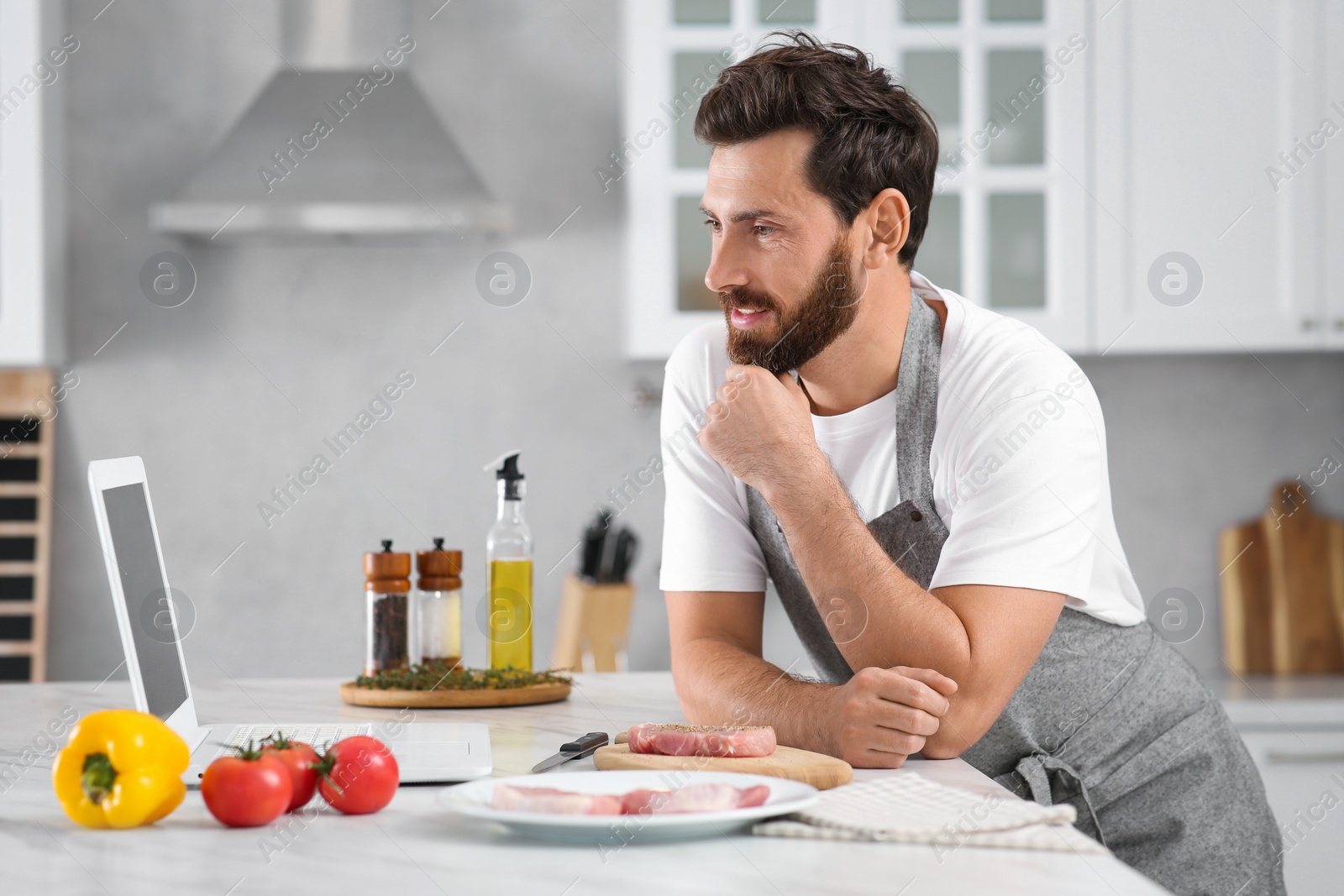 Photo of Man making dinner while watching online cooking course via laptop in kitchen