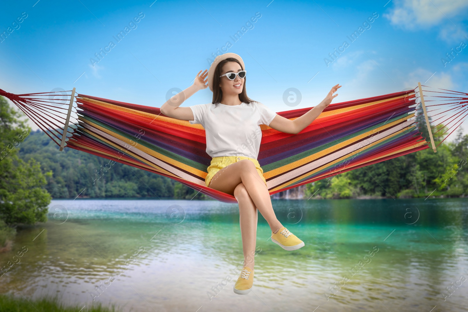 Image of Woman resting in hammock near river and mountains on sunny day 
