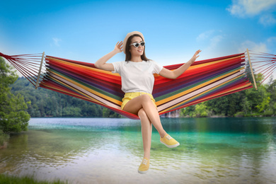 Woman resting in hammock near river and mountains on sunny day 