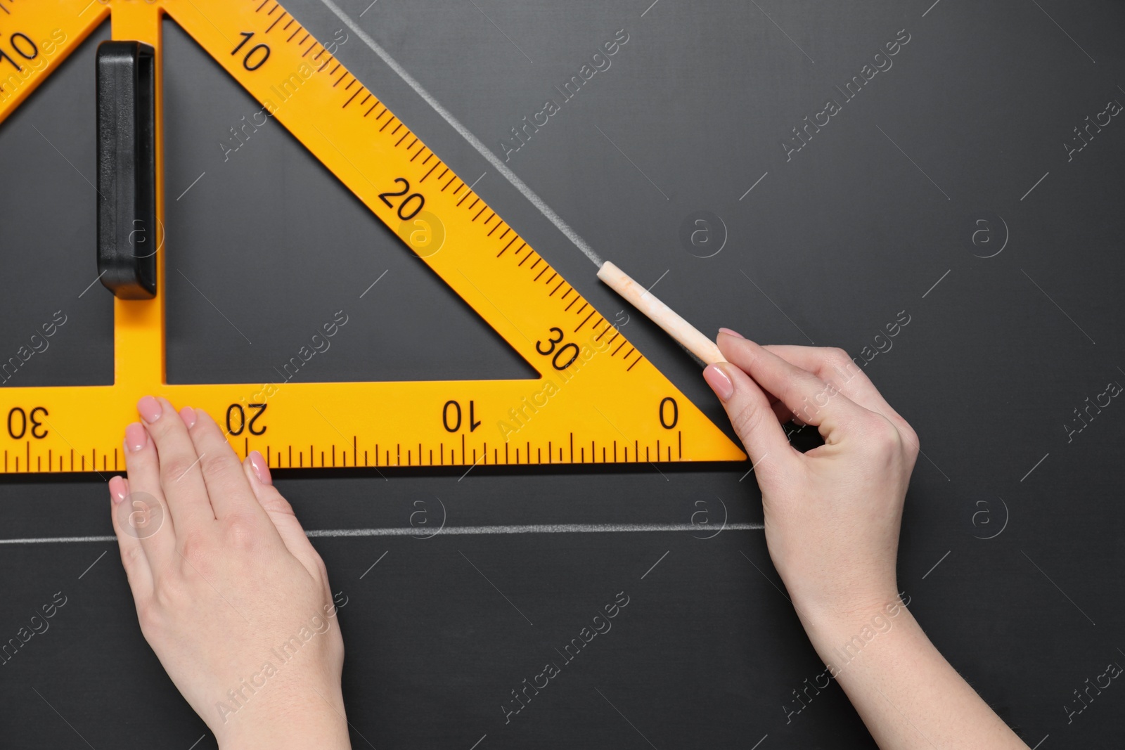 Photo of Woman drawing with chalk and triangle ruler on blackboard, closeup