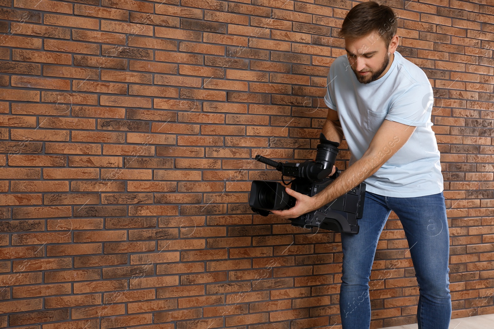 Photo of Operator with professional video camera near brick wall, space for text