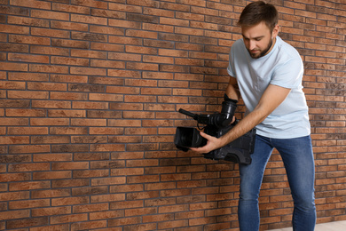 Operator with professional video camera near brick wall, space for text