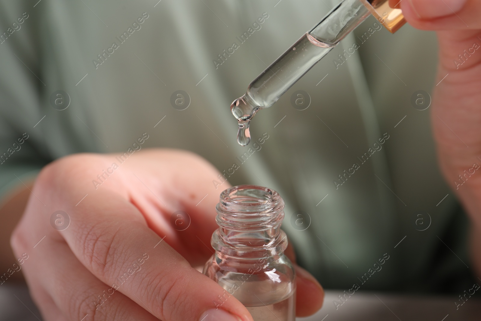 Photo of Woman with bottle of cosmetic serum at table, closeup