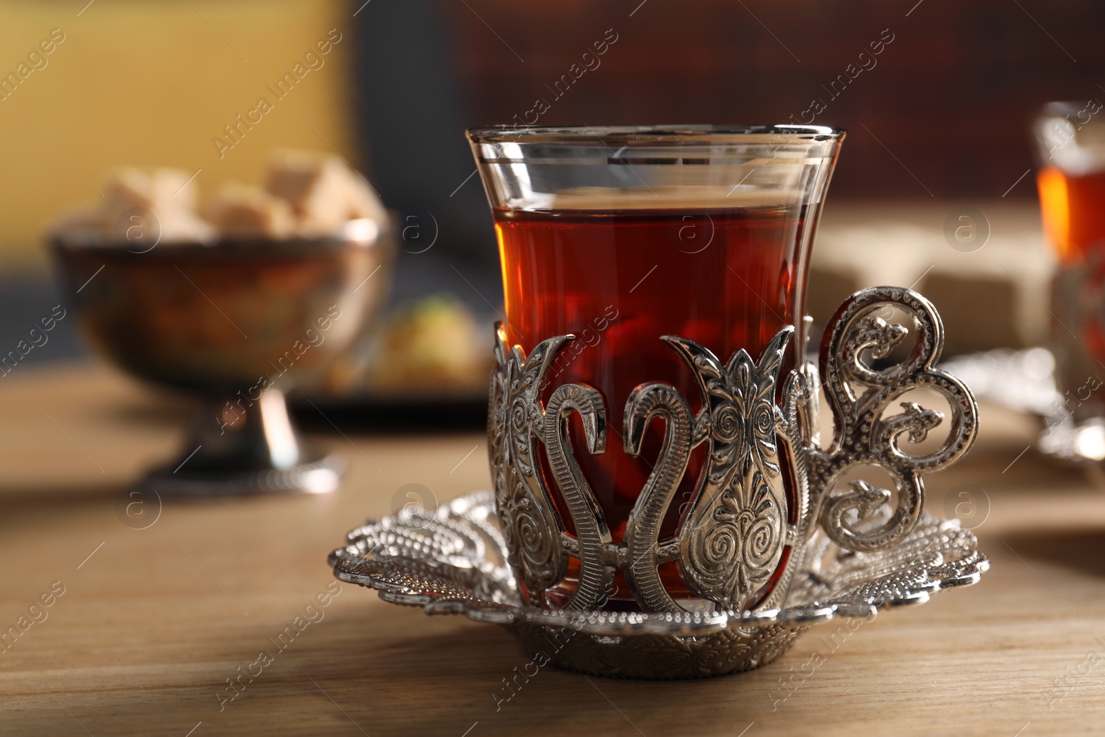 Photo of Glass of traditional Turkish tea in vintage holder on wooden table, closeup