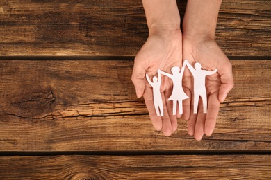 Photo of Woman holding paper figures of happy family in hands on wooden background, top view. Space for text