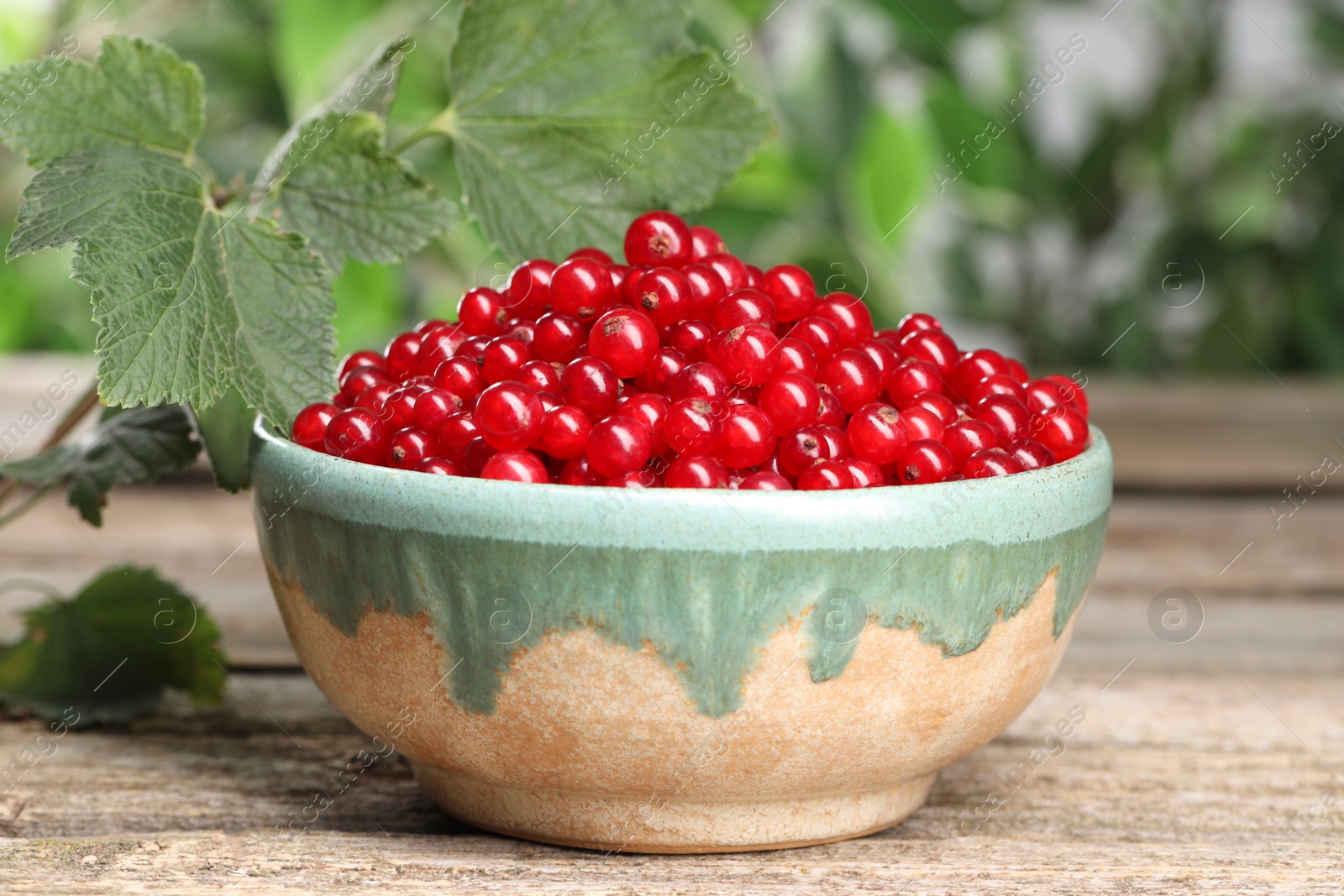 Photo of Ripe red currants in bowl and leaves on wooden table, closeup