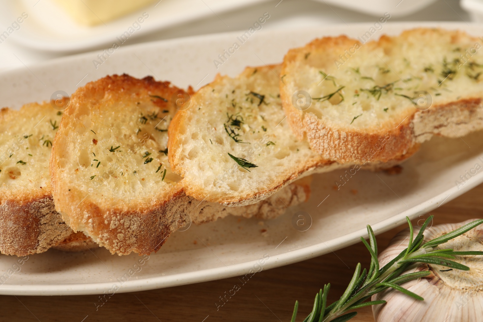 Photo of Tasty baguette with garlic, rosemary and dill on table