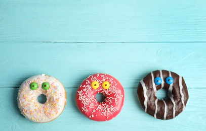 Photo of Delicious donuts decorated as monsters on light blue wooden table, flat lay with space for text. Halloween treat