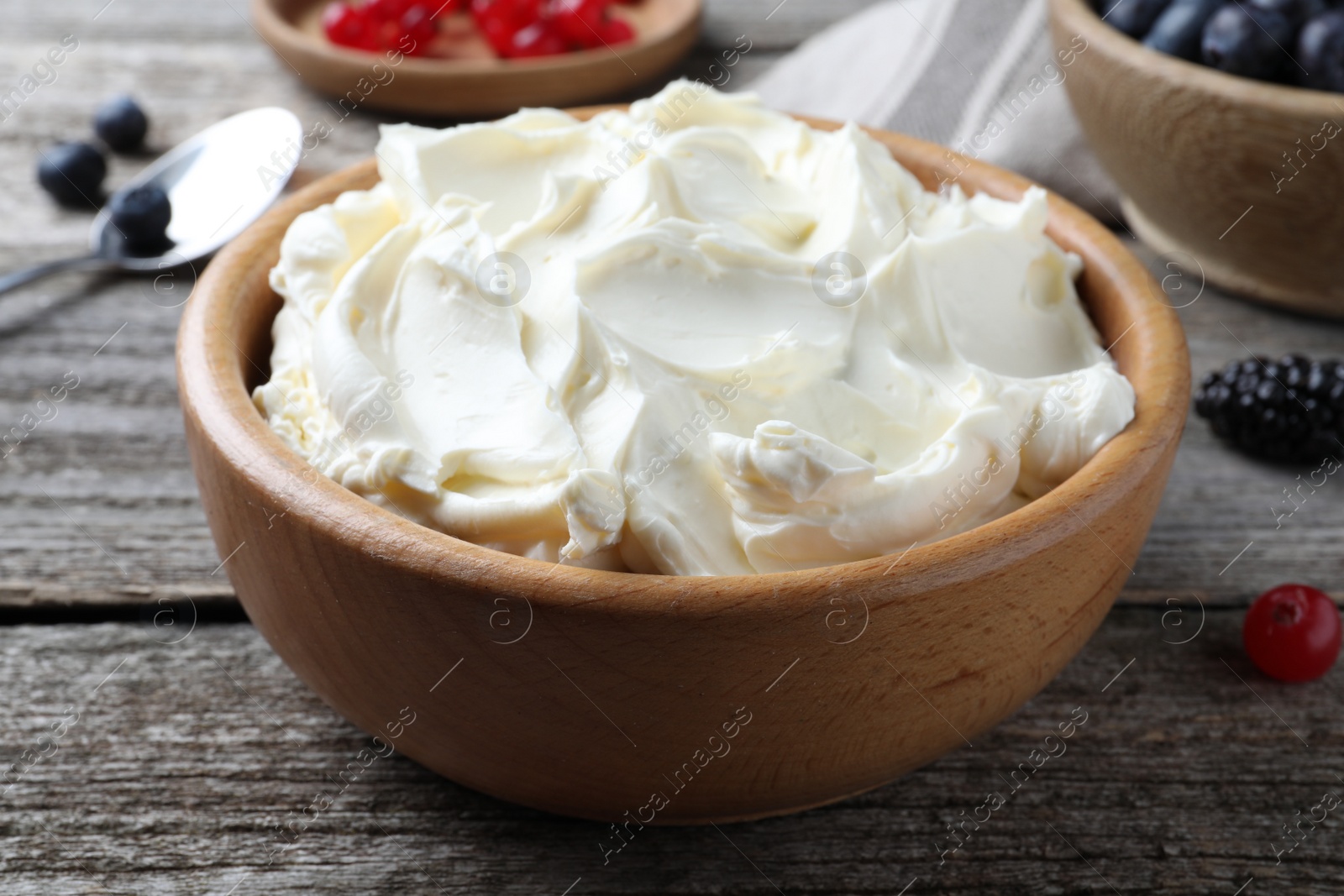 Photo of Tasty cream cheese and fresh berries on wooden table, closeup