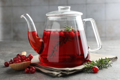 Photo of Tasty hot cranberry tea in teapot, rosemary and fresh berries on light grey textured table