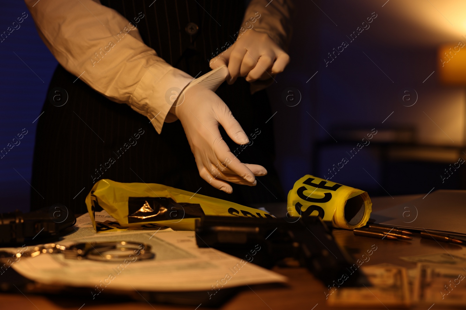 Photo of Professional detective in protective gloves working with evidence indoors at night, closeup