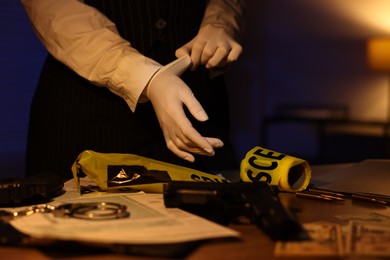 Photo of Professional detective in protective gloves working with evidence indoors at night, closeup