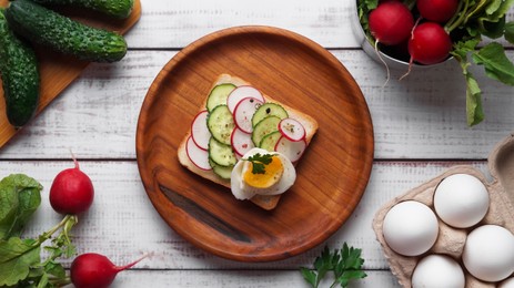 Photo of Tasty sandwich with boiled egg, radish, cucumber and ingredients on white wooden table, flat lay