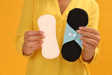 Photo of Young woman with reusable menstrual pad and pantyliner on yellow background, closeup