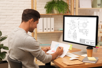 Male engineer working with technical drawing on computer in office