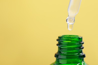 Dripping serum from pipette into bottle on yellow background, closeup. Space for text