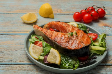 Photo of Tasty salmon steak with lemon and vegetables on white wooden table, closeup