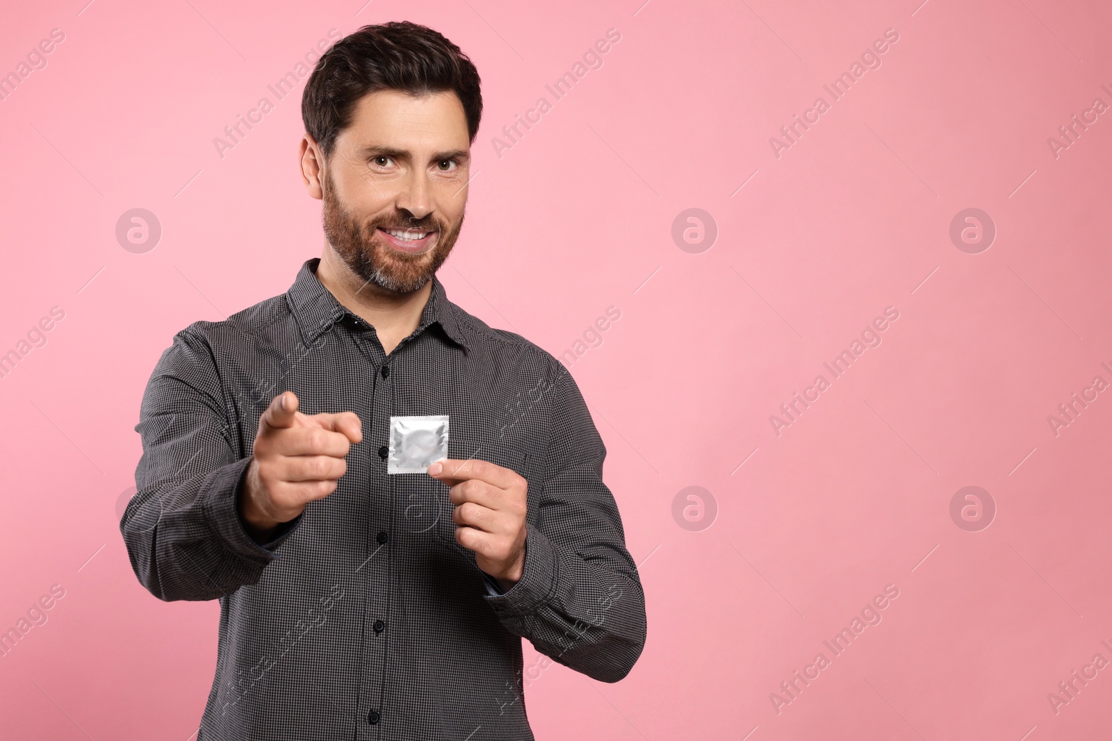 Photo of Happy man holding condom on pink background, space for text. Safe sex