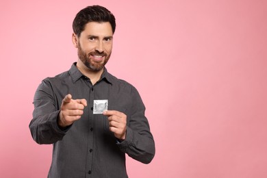 Photo of Happy man holding condom on pink background, space for text. Safe sex