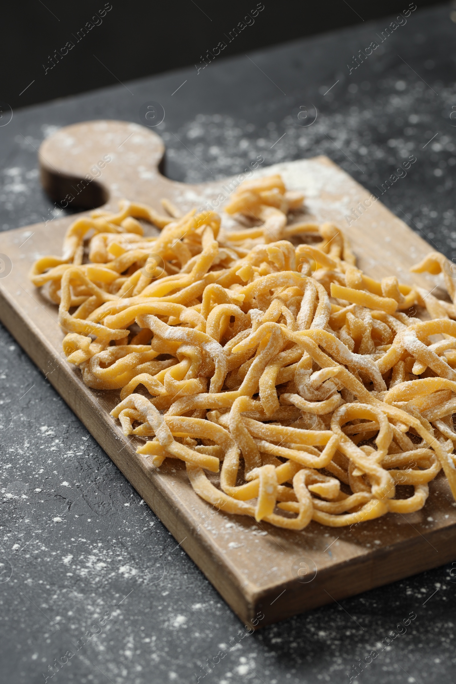 Photo of Board with homemade pasta and flour on dark table