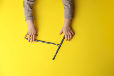 Photo of Little kid holding drumsticks on yellow background, top view
