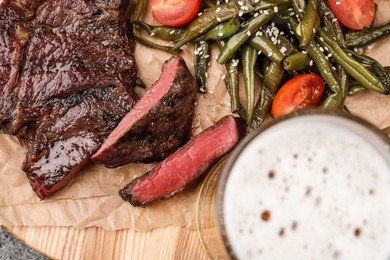 Photo of Mug with beer, delicious fried steak and asparagus on wooden table, closeup