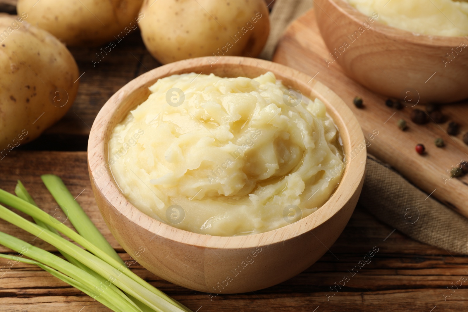 Photo of Bowls of tasty mashed potato, pepper and leeks on wooden table, closeup