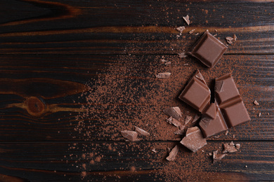 Delicious milk chocolate and cocoa powder on wooden table, flat lay. Space for text