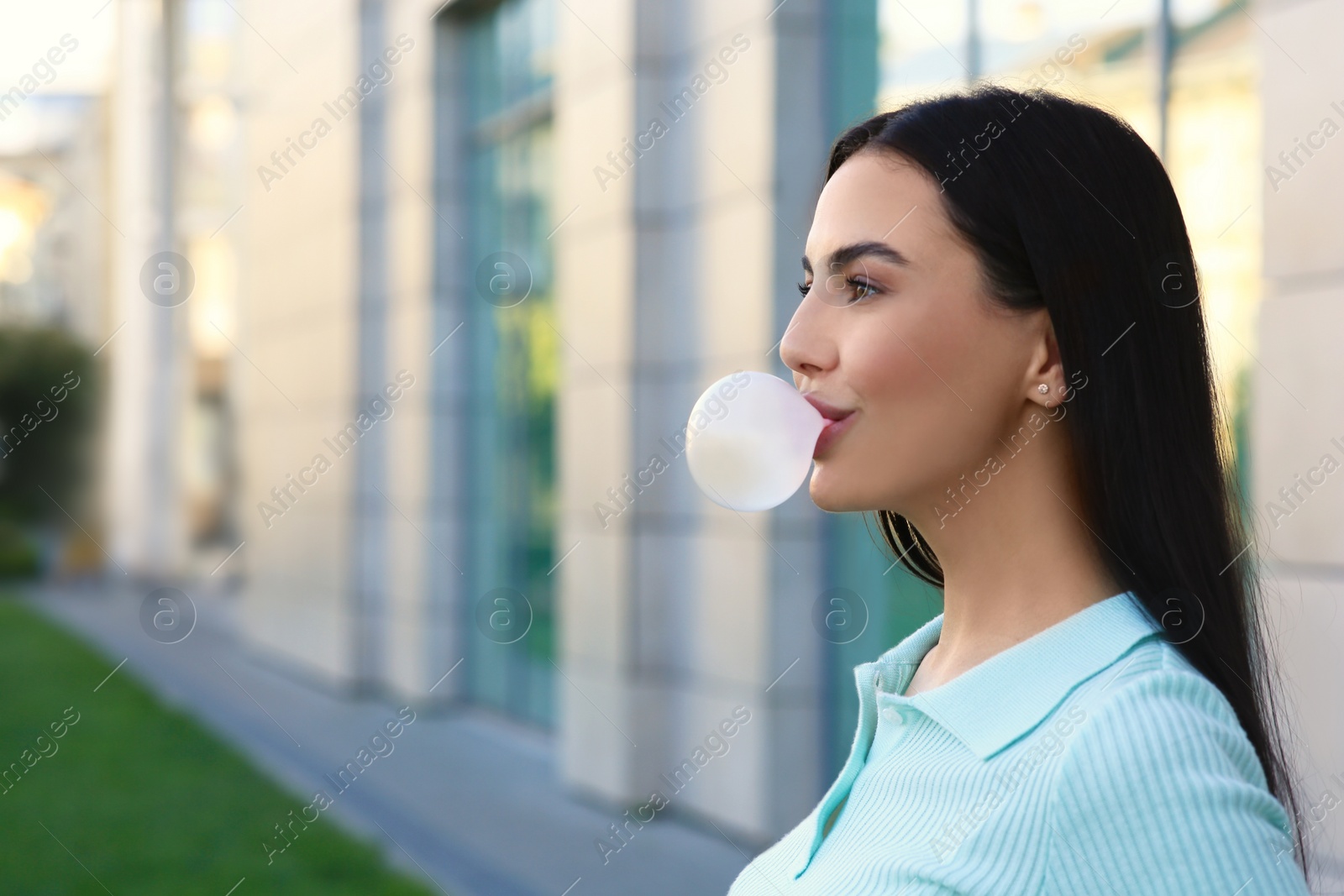 Photo of Beautiful woman blowing gum near building outdoors, space for text