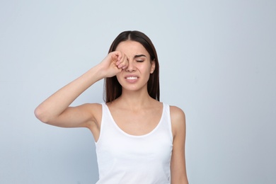 Photo of Young woman rubbing eye on light background. Annoying itch