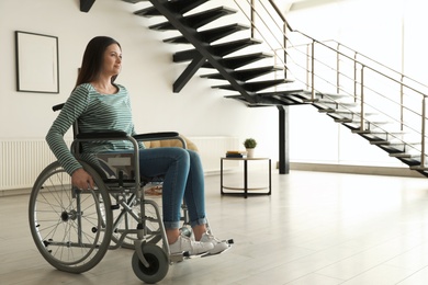Young woman in wheelchair indoors. Space for text