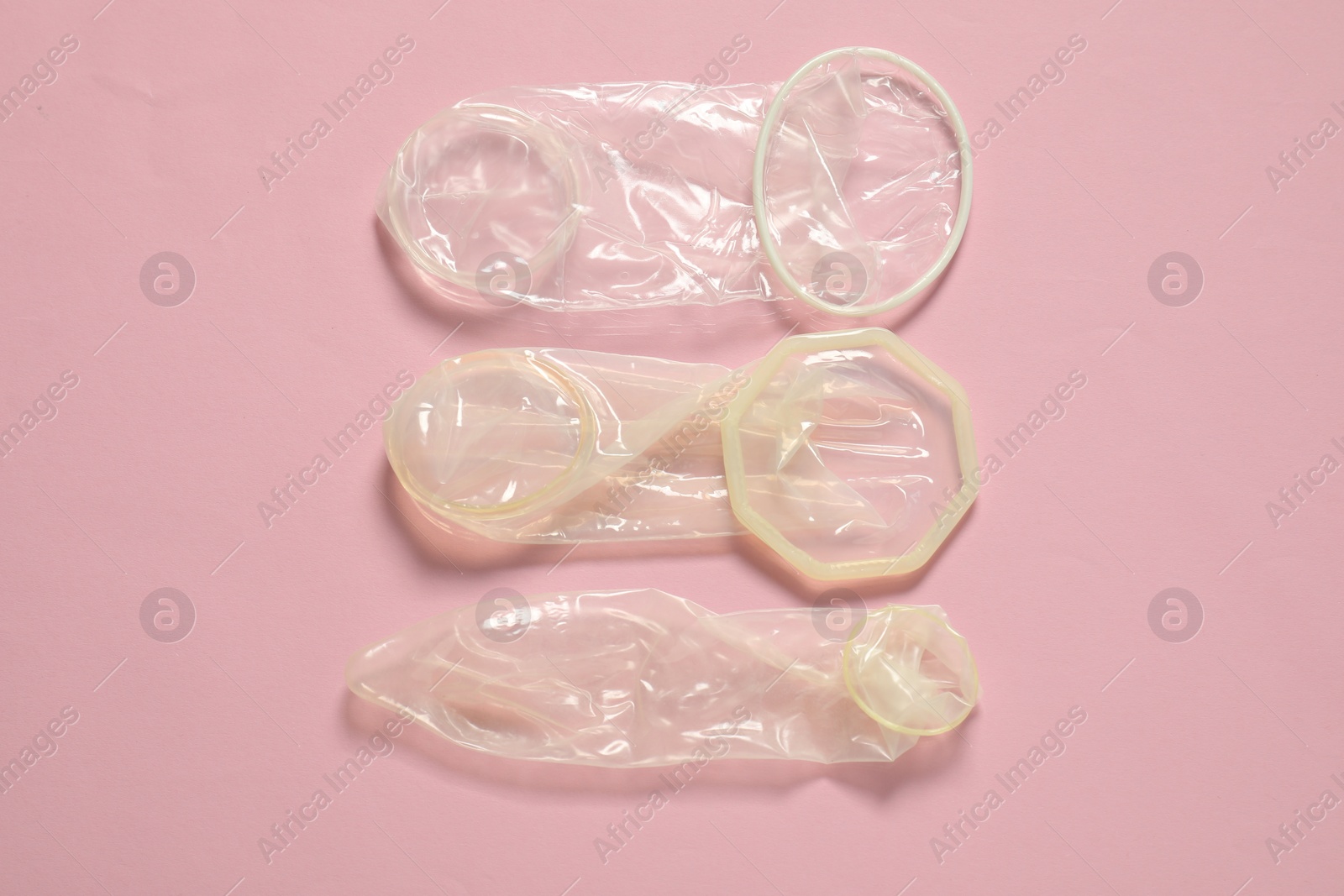 Photo of Unrolled female and male condoms on light pink background, flat lay. Safe sex