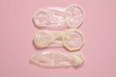 Unrolled female and male condoms on light pink background, flat lay. Safe sex