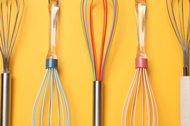 Different whisks on yellow background, flat lay