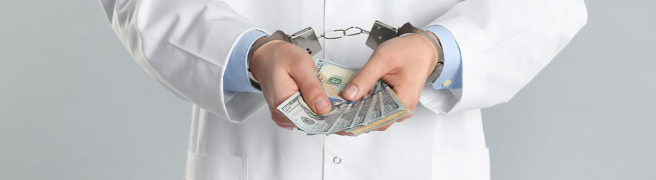 Image of Doctor in handcuffs with bribe on grey background, closeup. Banner design