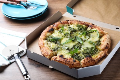 Photo of Delicious pizza with pesto, cheese and arugula in cardboard box served on wooden table
