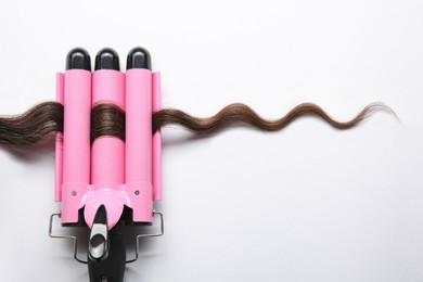 Photo of Modern triple curling iron with brown hair lock on white background, top view