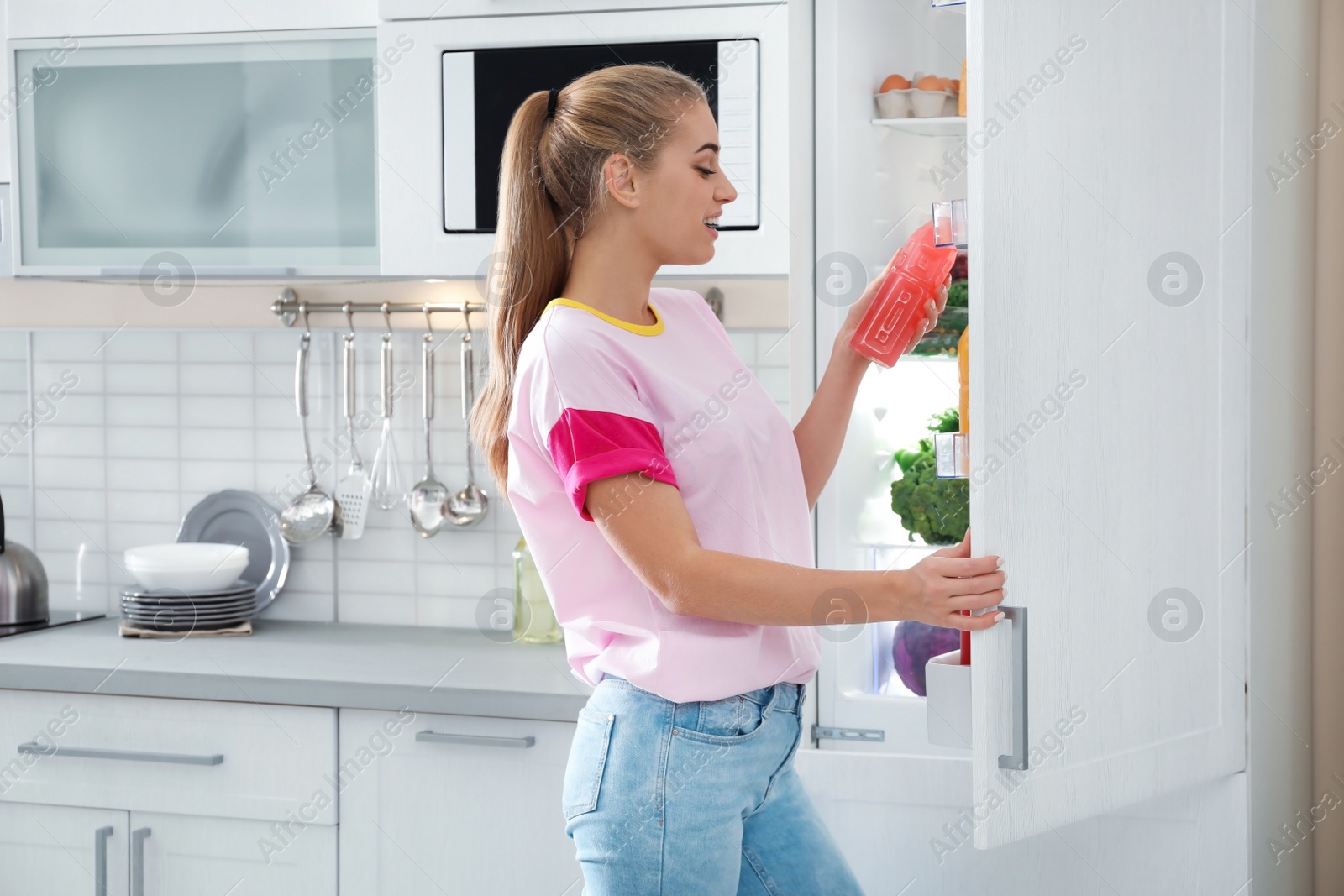 Photo of Woman taking bottle of juice out of refrigerator in kitchen