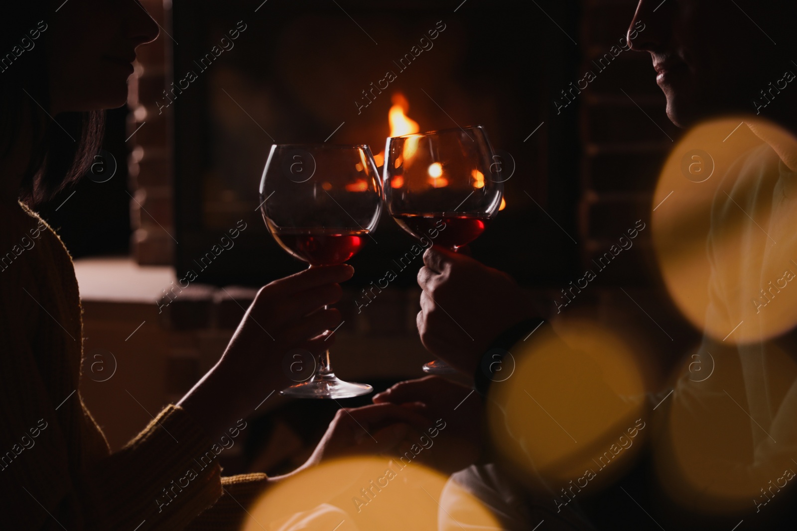 Photo of Couple with glasses of red wine near burning fireplace, closeup