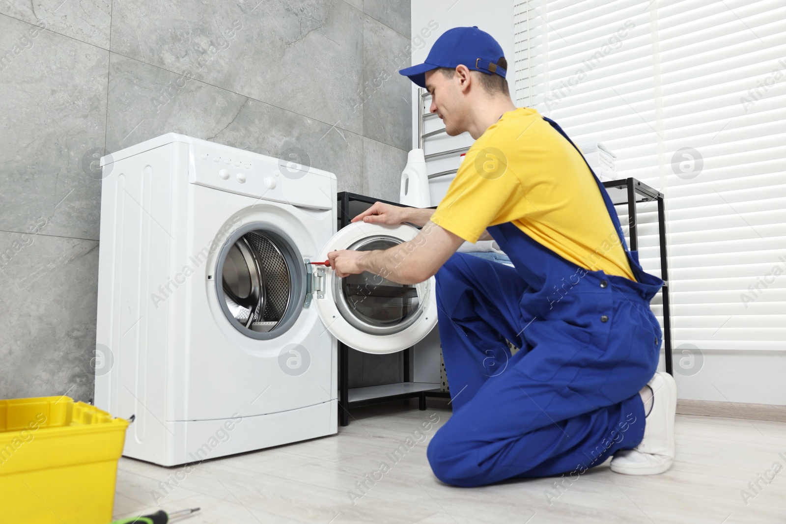 Photo of Plumber repairing washing machine in bathroom, low angle view