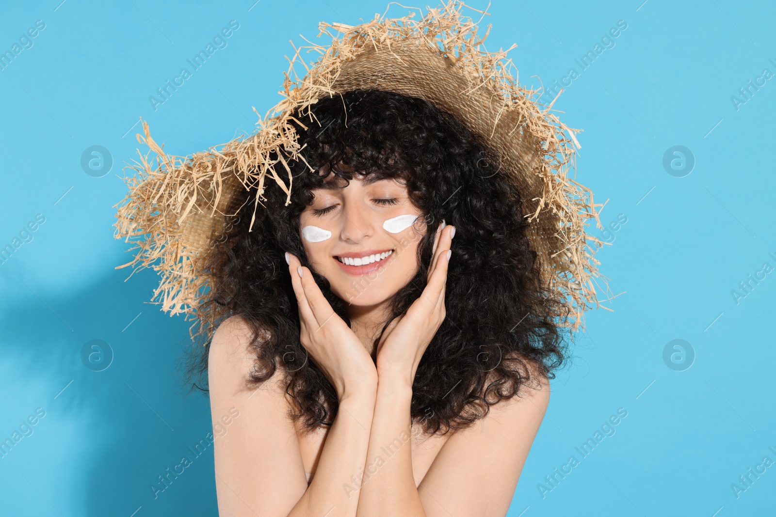 Photo of Beautiful young woman in straw hat with sun protection cream on her face against light blue background