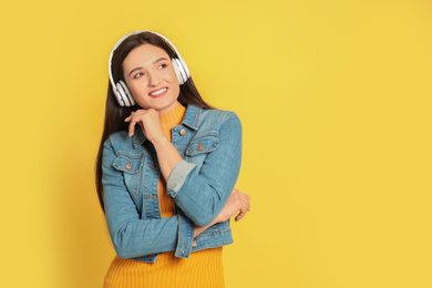 Young woman listening to audiobook on yellow background. Space for text